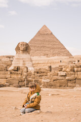 little boy sitting on knees at background of Great Sphinx and Chephren's pyramid in Giza, Egypt