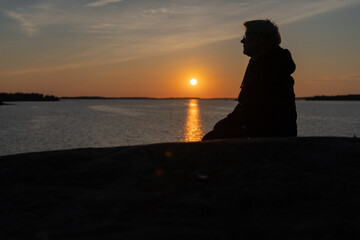 A woman sits on the rocks, on the seashore, he looks at the sunset,. The concept of rest, vacation.
