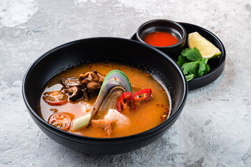 Traditional spicy Thai soup Tom Yum with shrimp and seafood in ceramic bowl on stone background