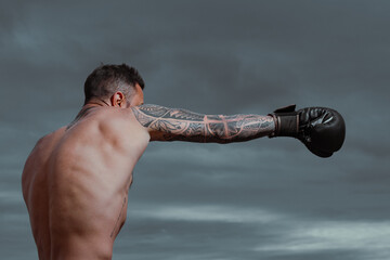Boxer in a fight. Fist fight. Strong man with tattooed body boxing outdoor. Man with muscular body...