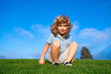 Fototapeta premium Portrait of a smiling little boy lying on green grass. Smiling boy having fun outdoor in spring garden.