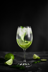 A wine glass of fresh cold lemonade with ice, cucumber slices and lime fruit on  the dark background