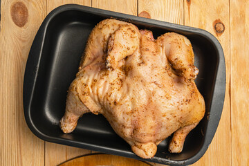 Close-up of a spiced chicken carcass lying in a black baking pan on a wooden background. Close-up. Preparing to cook the bird in the oven.