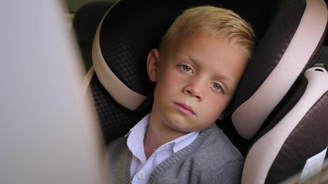 Close-up of a sad little schoolboy sitting in a car in a car seat, being bullied at school.