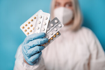 Close up of female doctor looking at camera wearing face mask holding pill blisters antiviral drug...