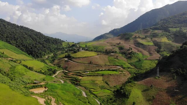 Wide slow moving aerial shot of beautiful green valley with terraced fields and winding road. Huoi Dap, Vietnam