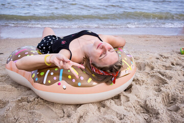 a young girl lies with her back on an inflatable circle on the beach by the sea