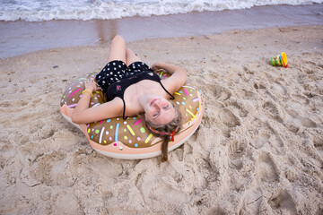 a young girl lies with her back on an inflatable circle on the beach by the sea