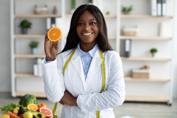 Vitamin C is good for immunity. Happy african american dietologist holding orange half, recommending fresh fruits to eat