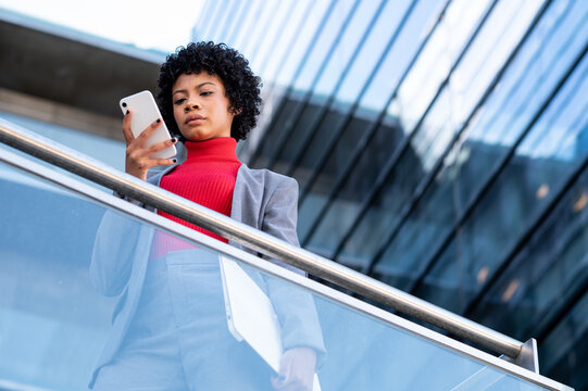 Elegante mujer afroamericana utilizando el tel&eacute;fono m&oacute;vil en un edificio de oficinas 