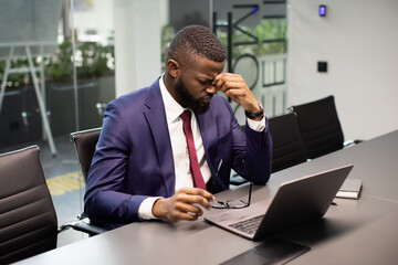 Obraz premium Exhausted black manager sitting at office, having headache