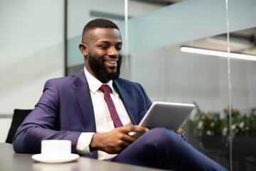 Fototapeta na wymiar Cheerful black businessman using digital tablet at office, copy space