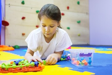 a child a girl on the floor of a children's rehabilitation center for correction collects a chain of viruses from a toy. the concept of lifestyle