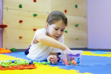 Fototapeta premium a child a girl on the floor of a children's rehabilitation center for correction collects a chain of viruses from a toy. the concept of lifestyle