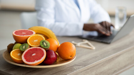 Nutritionist desk with healthy fruits and caliper, dietitian working on laptop, sitting at workplace, selective focus