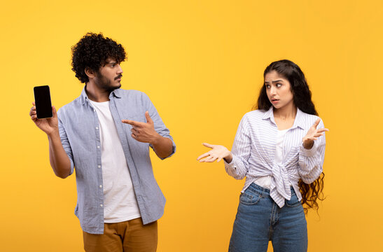 Cheating Concept. Angry Indian Man Checking His Girlfriend Cellphone And Asking Lady For Explanation