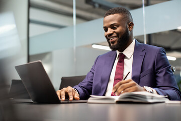 Smiling african american businessman using notebook and taking notes