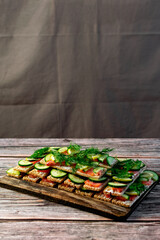 Sandwiches with red salmon fish on thin wheat bread for dietary nutrition, fresh cucumber, lemon and dill greens are visible in the composition, a large stack on a wooden board