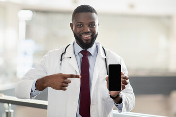 Handsome african american doctor pointing at smartphone, mockup