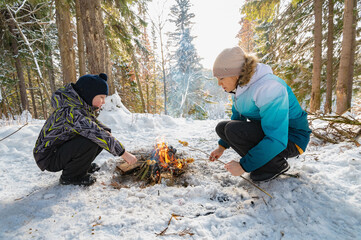 A woman and a boy around a campfire in winter in the forest fry dumplings on skewers. - 488946520