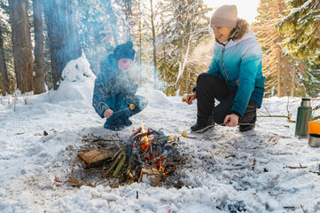 A woman and a boy around a campfire in winter in the forest fry dumplings on skewers. - 488946521
