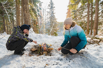 A woman and a boy around a campfire in winter in the forest fry dumplings on skewers. - 488946522