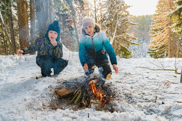 A woman and a boy around a campfire in winter in the forest fry dumplings on skewers. - 488946523