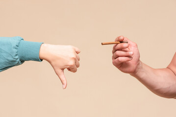 Male hand with a cigarette and woman hand which is showing a thumbs down gesture sign. No smoking concept.