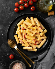 Tortiglioni with tomatoes, ricotta and basil in a black plate on a dark kitchen table. Traditional Italian pasta with vegetables and creamy cottage cheese on a culinary background. Top view