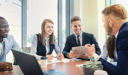 Young handsome man gesturing and discussing something while his coworkers listening to him sitting at the office table.