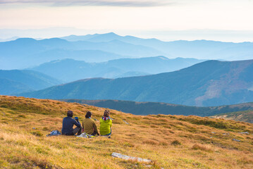 Group of hikers sitting on a hill and enjoy carpathian mountain valley