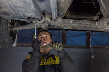 Young mechanic working hard under the car in workshop garage