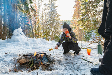 A woman and a boy around a campfire in winter in the forest fry dumplings on skewers. - 488949369