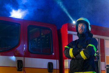 Fototapeta na wymiar Low angle view of firefighter with fire truck in background at night.