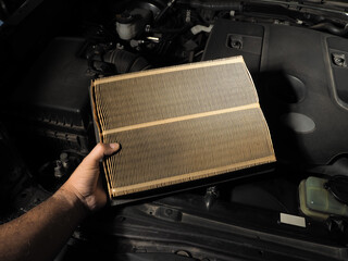 A mechanic holds a car air filter in his hand for auto maintenance in a repair shop, automotive...