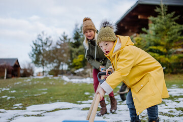 Obraz premium Boy with Down syndrome with his mother clearing snow from path with shovel in front of house.