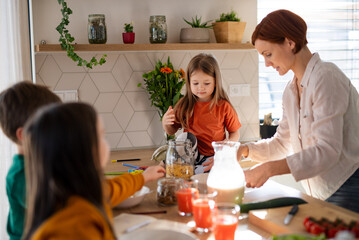 Mother of three little children preparing breakfast in kitchen at home.