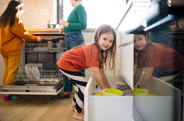 Three little chidlren helping with dishes in kitchen at home.