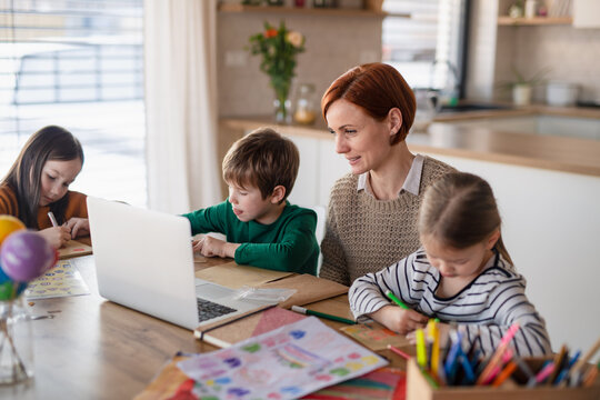 Mother of little children supervising them when distance learning and doing homework at home.