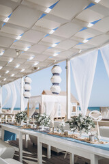 restaurant hall on the sea coast, decorated with paper lamps and white fabrics. tables are decorated with floral arrangements of white flowers