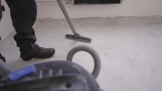 The master with the help of a vacuum cleaner removes dust from the floor. Removing dust at a construction site with an industrial vacuum cleaner. A man uses an industrial vacuum cleaner indoors.