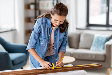 repair, diy and home improvement concept - happy smiling woman with ruler and pencil measuring wooden board at home