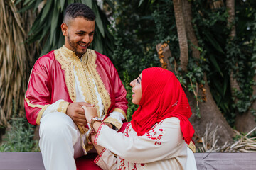shot of a cute couple dressed with arab clothes looking each other in a public park with palm trees in the background