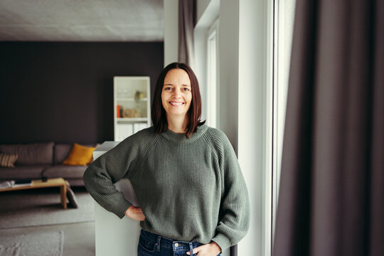 Portrait of smiling woman standing by window at home