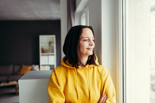 Smiling woman looking out through window day dreaming at home