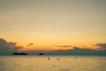 People floats on stand up paddle boards against the backdrop of a spectacular colorful sunset over sea and islands on a summer evening. 