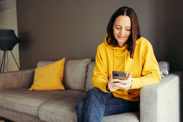 Woman wearing yellow hood sitting with smart phone on sofa at home