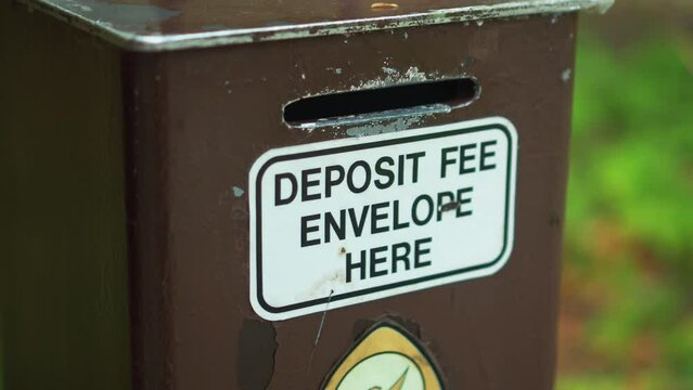 Closeup of heavy duty outdoor campground cash money fee collection post with deposit envelope slot sign at camping site in nature
