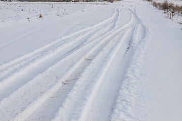 Snowy road in a field leading to pine forest. Winter road to nowhere in sunny day, snow-covered fresh car track. Car traces in a deep snow of remote rural area