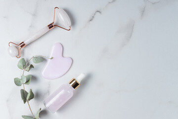 Rose quartz massage roller and gua sha stone scraper tools and dry eucalyptus on marble background. Flat lay, top view aesthetic beauty skin care wellness treatment concept